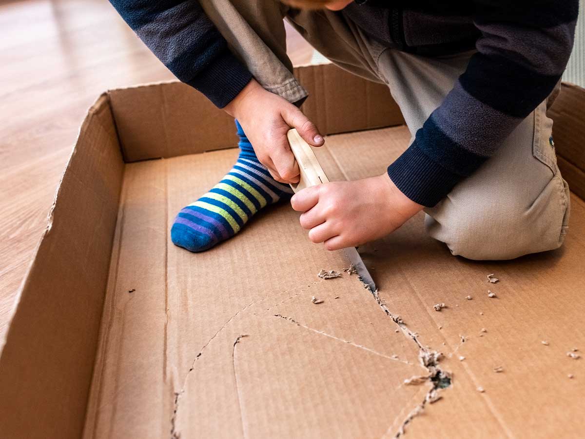 A close up image of a child using a mini saw to cut a piece of cardboard in the shape of a Viking shield.