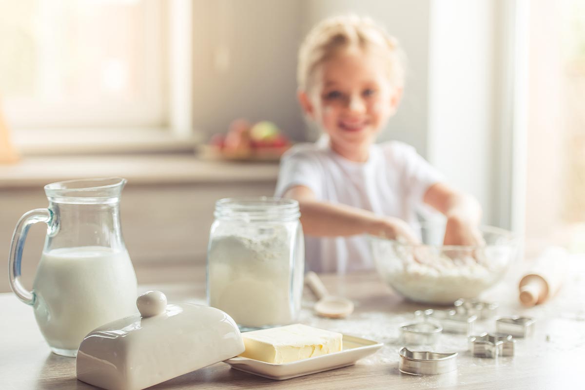 A young girl is mixing ingredients to make a butterfly cake, in the foreground there are butterfly cake ingredients: butter, flour and milk.