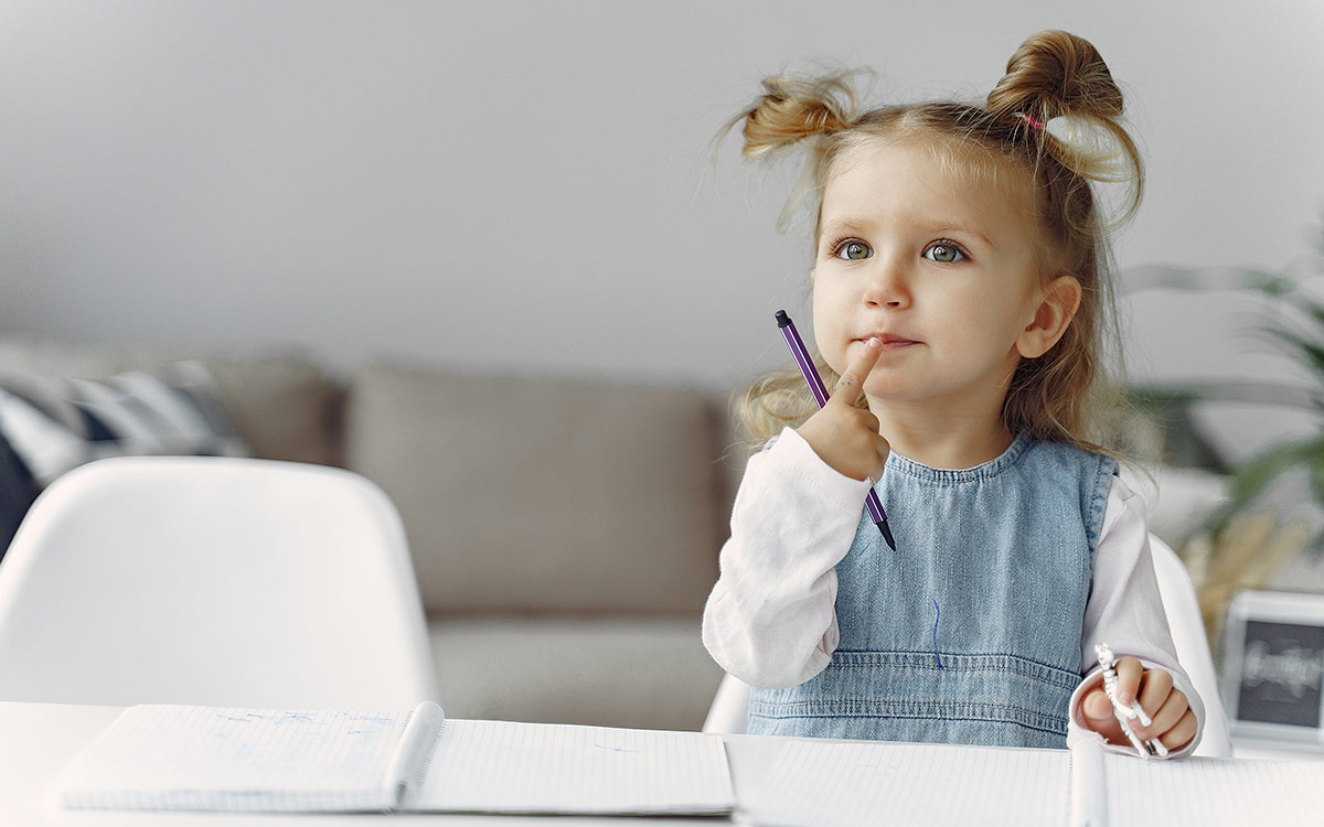 Young girl sat at the table thinking as she learns about prefixes and suffixes.