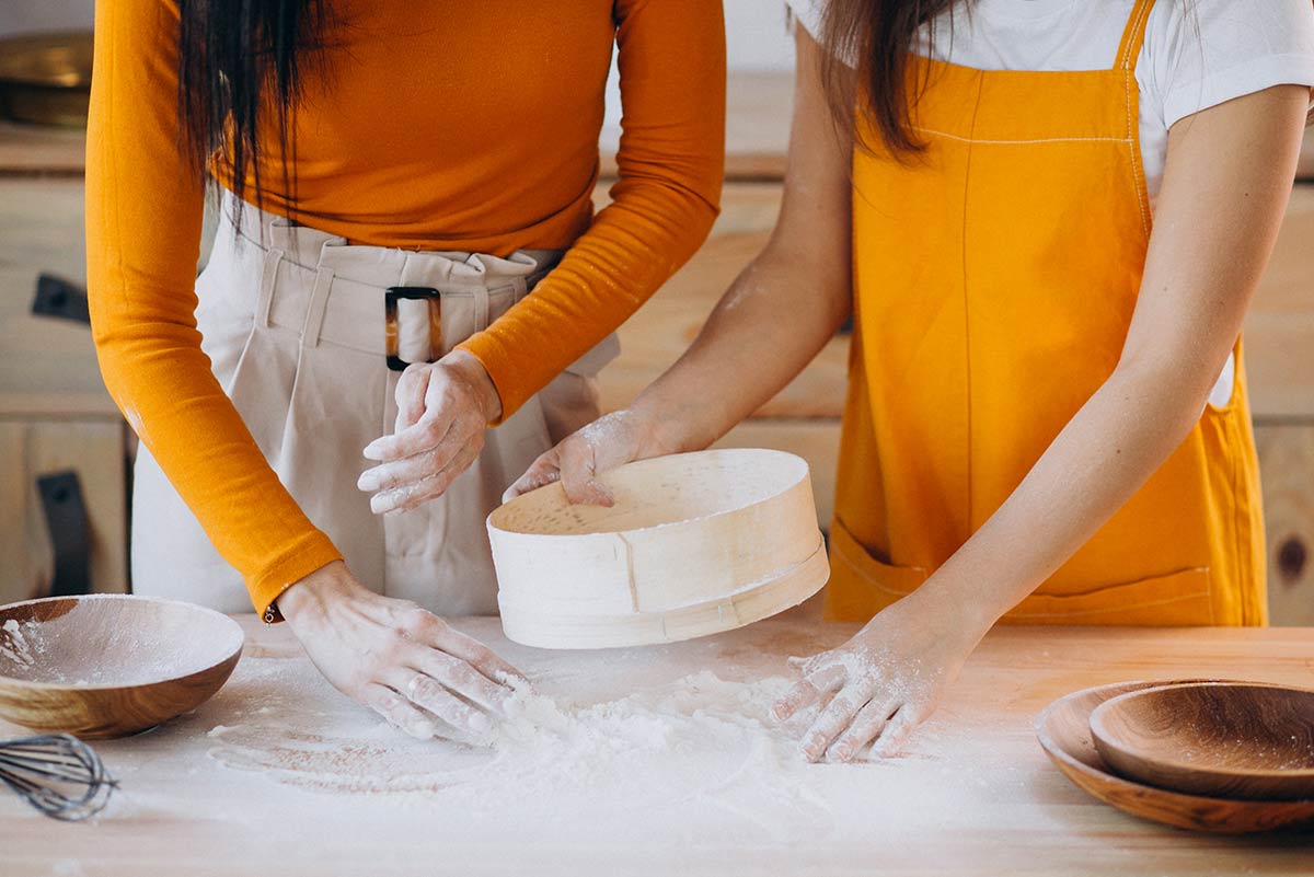 A close up image of a mother and daughter sifting flour to make a burger cake.