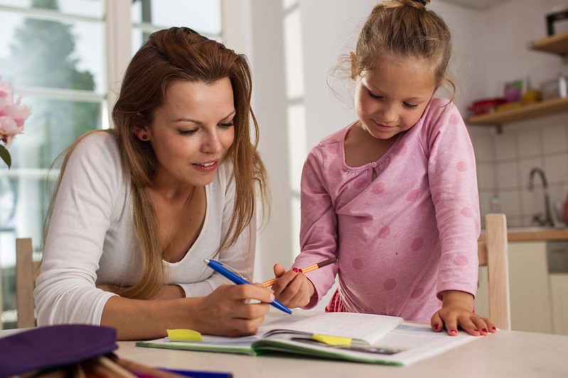 A mother and daughter are sat together learning about the present perfect tense, they have a pile of books in front of them.