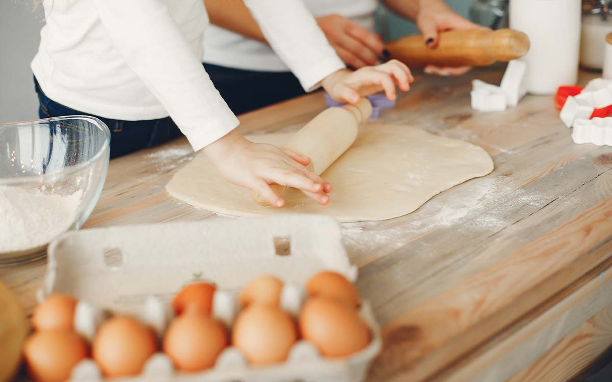 A close up image of a child, with the help of an adult, using a rolling pin to prepare ingredients for a snake cake.