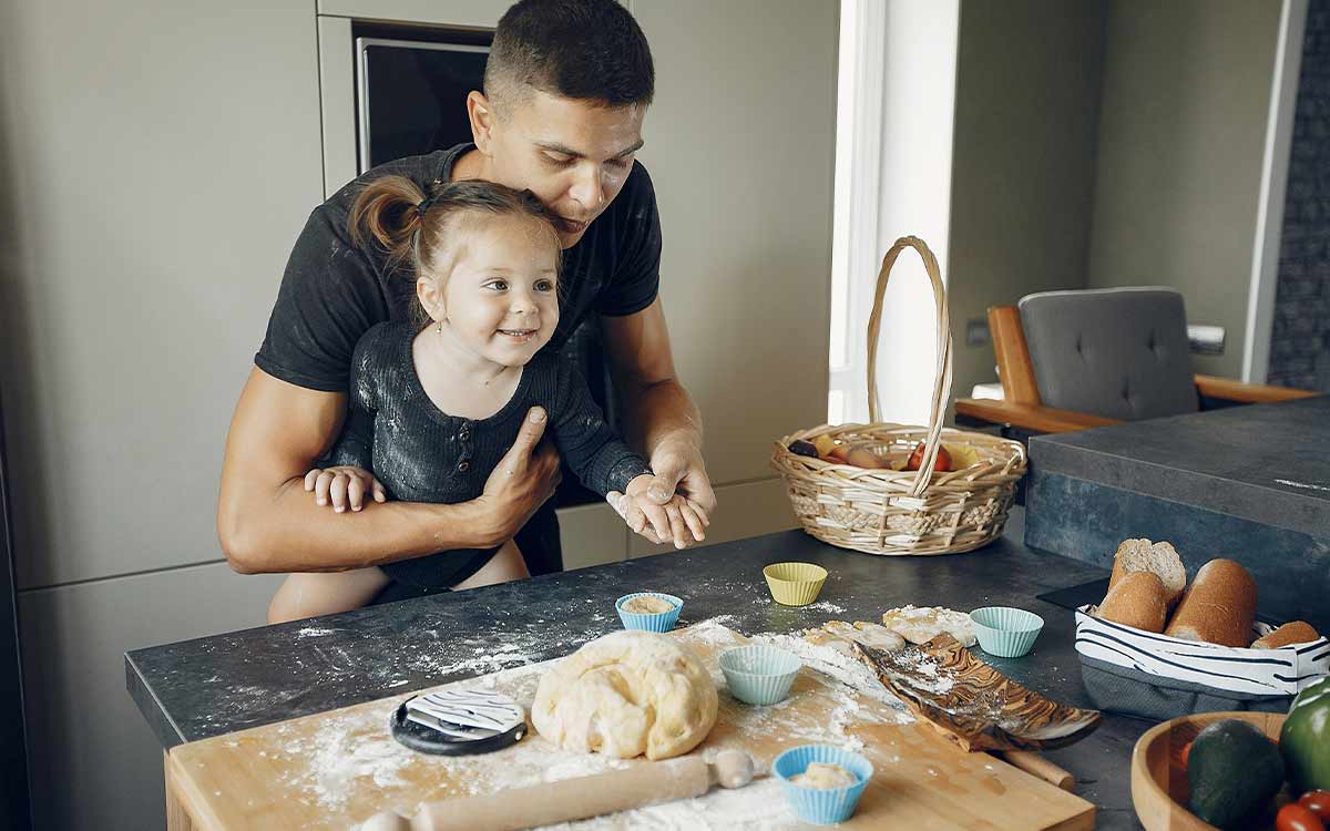A little girl is lifted up by her father as she helps to make a snake cake.