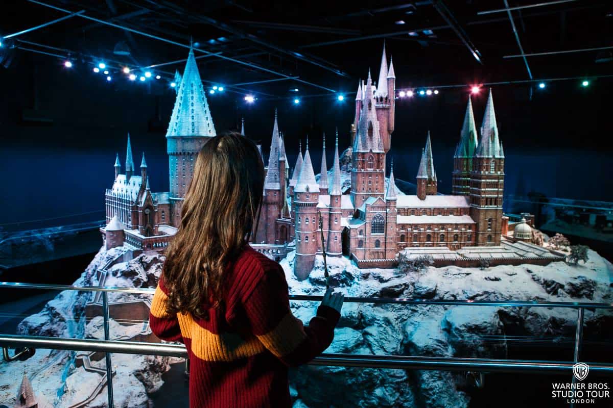 Young girl, dressed in a Gryffindor jumper and holding a wand, looking at the Hogwarts model at the studio tour.