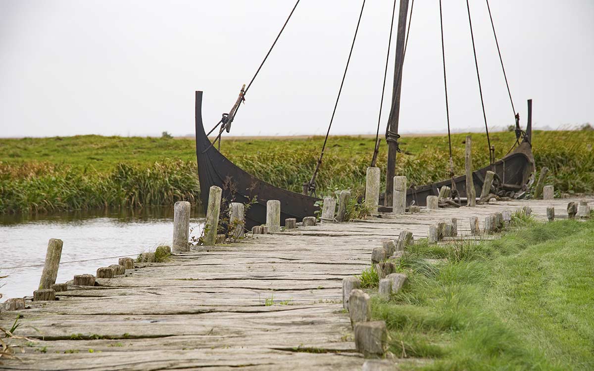 A Viking boat in a river with a green field behind it.