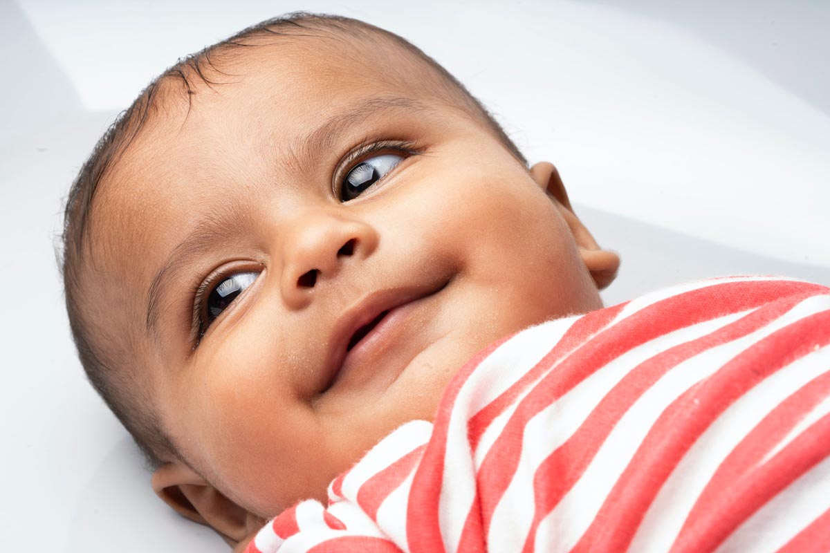 A baby wearing a red and white striped t shirt lies on his back and looks to the side.