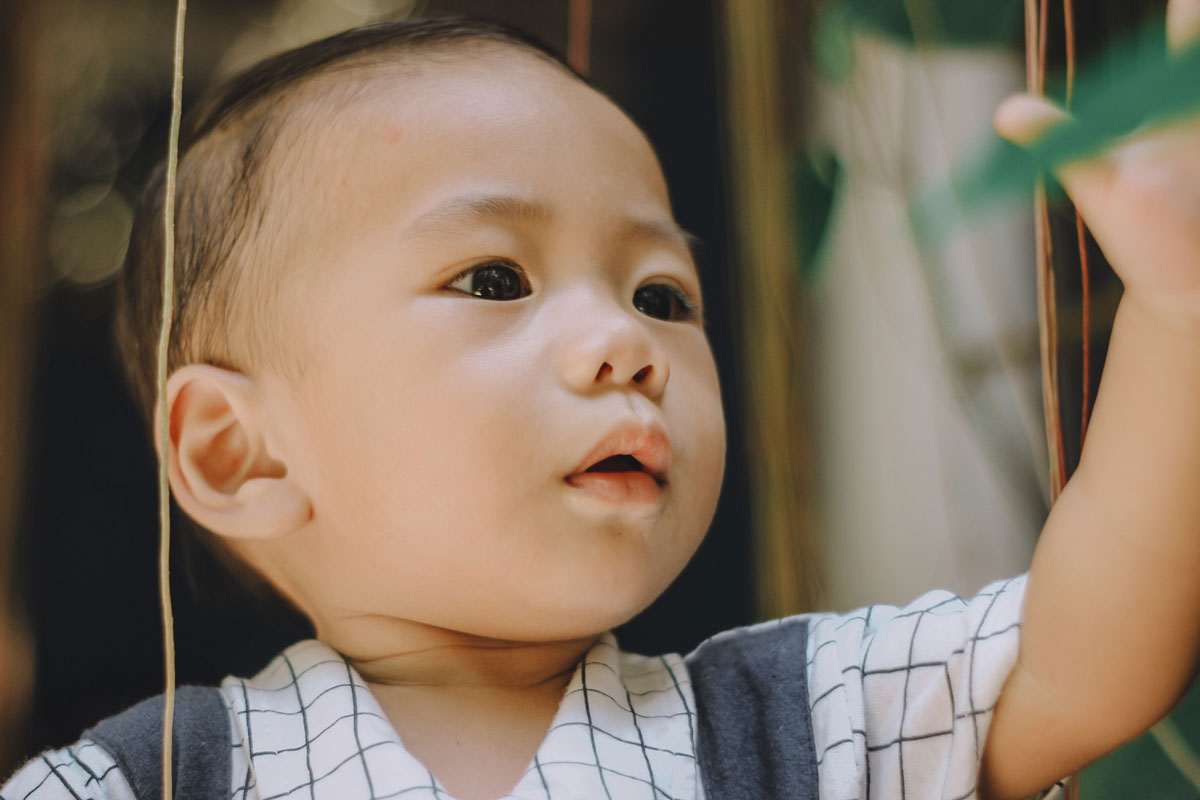 A baby boy reaches his hand out to grab something in front of him.