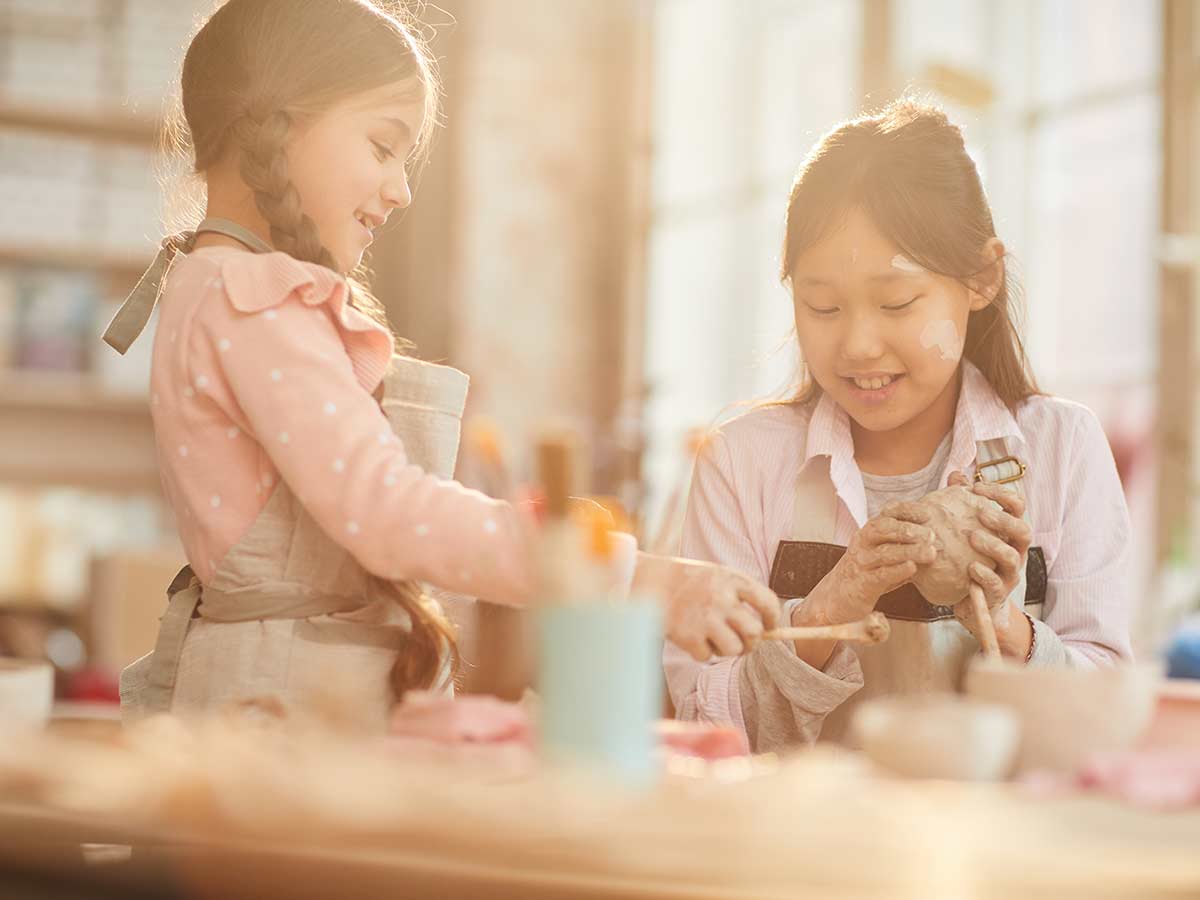 Two girls smile as they sit at a craft table together using clay to make a giraffe craft.