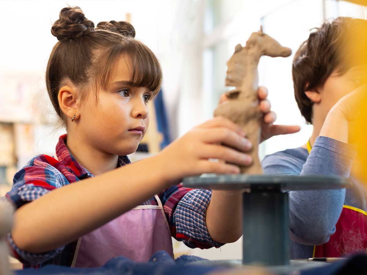 A young girls concentrates as she shapes some clay into the shape of a giraffe.
