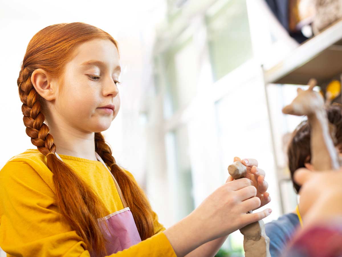 A girl makes a giraffe's head out of clay to complete her giraffe craft.