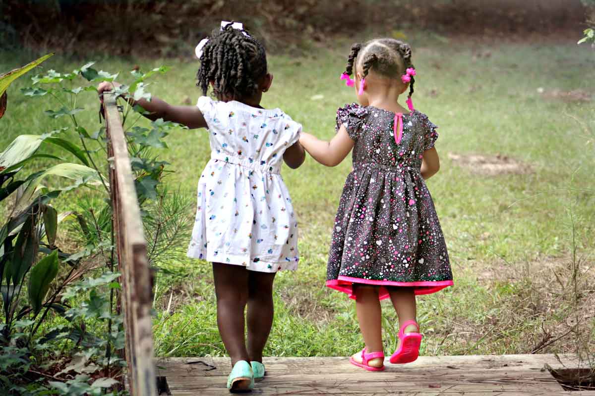 Two little girls walking hand in hand in the park.