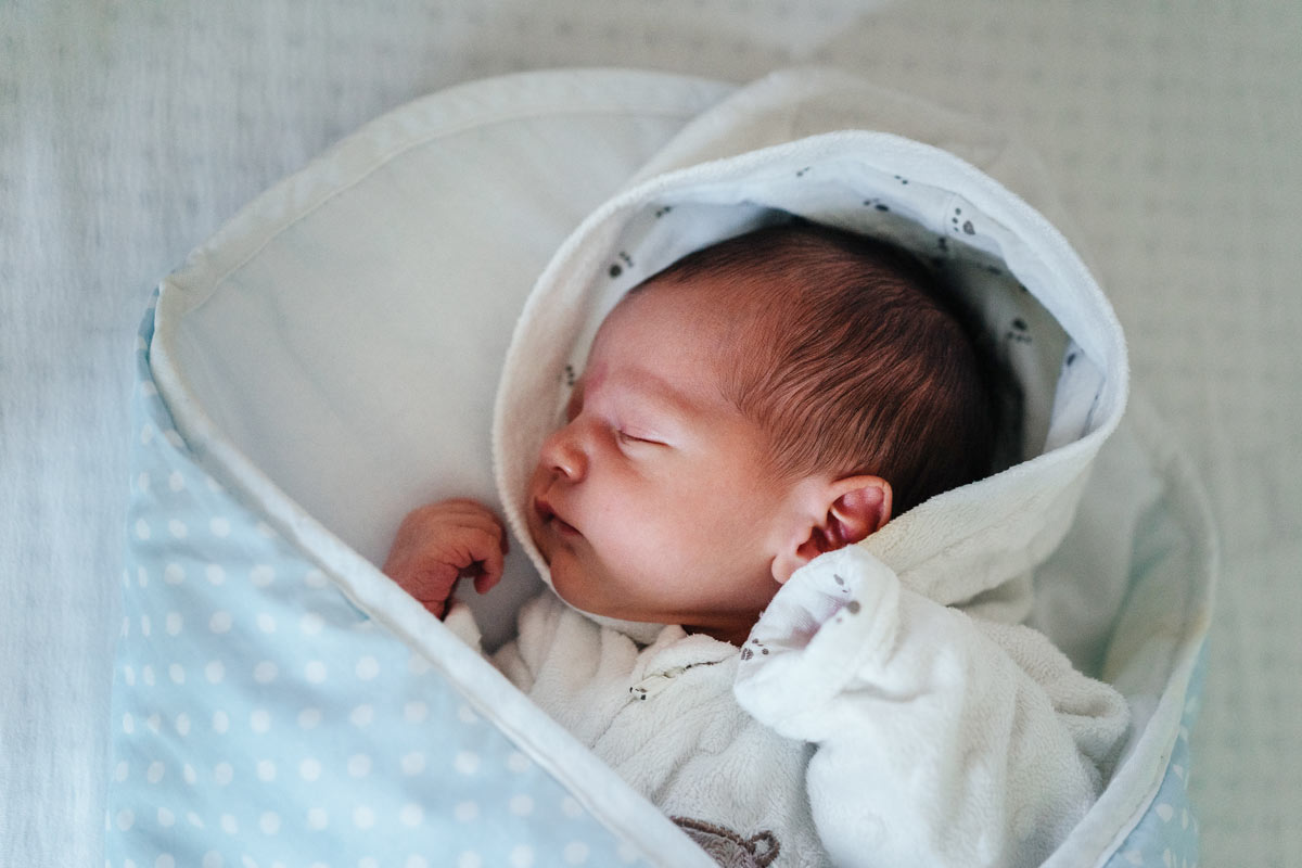 Newborn baby sleeping wrapped in a blue and white polka dot blanket.