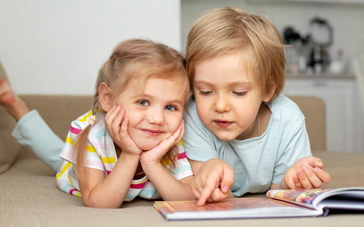 Young brother and sister lying on the sofa reading a book together.