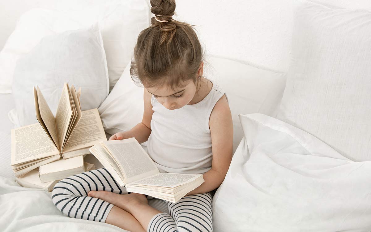 A KS2 girl sat on the sofa reading a book to help her learn about the possessive apostrophe.
