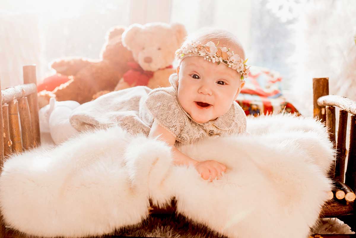 Baby girl wearing a flower headband lying on her tummy on a fluffy blanket.