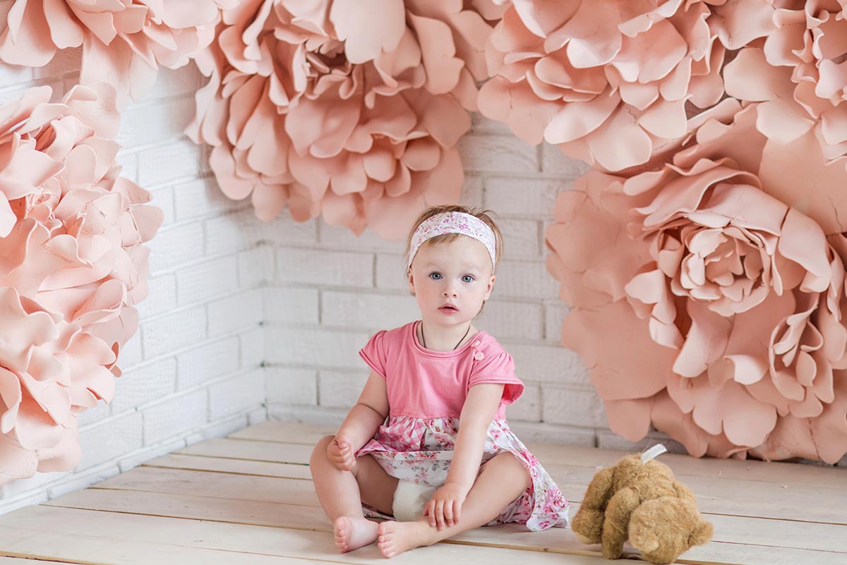 Little girl wearing pink sat on the floor surrounded by pink flower decorations.