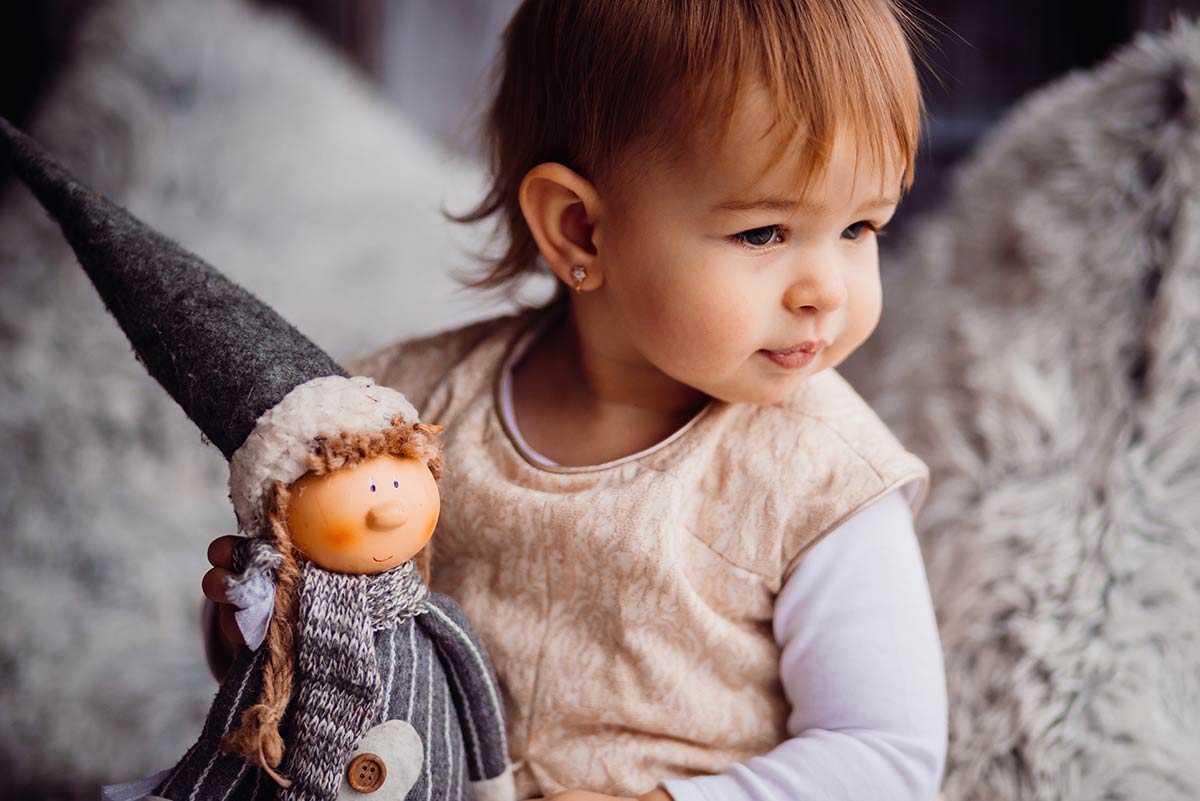 Baby girl holding an edgy toy with a long hat, looking off to the side.