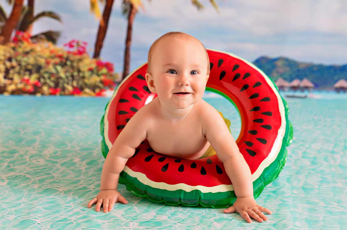 Baby boy wearing an inflatable watermelon ring crawling in the water.