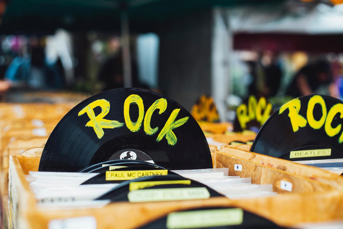 A black vinyl disc with 'rock' written on it in bright yellow is pictured amongst boxes of vinyls in a record store.