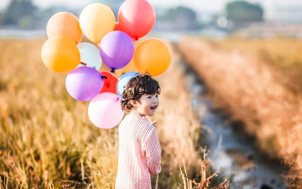 Young girl walking in a field holding bunch of colourful balloons - an example of how gases work for KS2 kids.