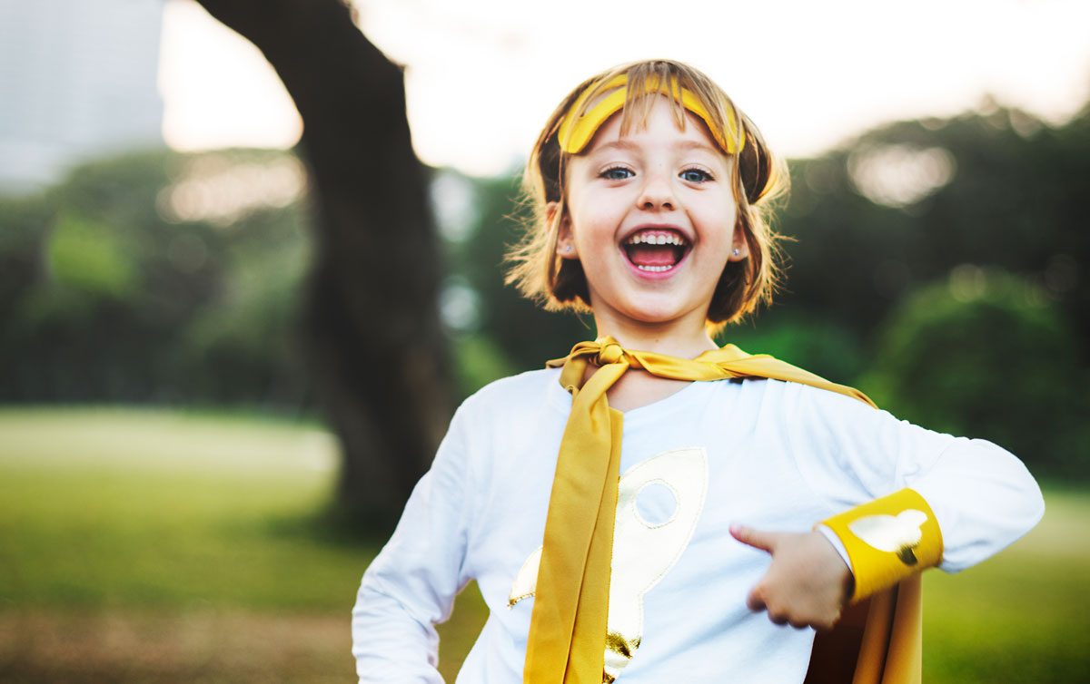 A young boy who is dressed in a yellow superhero costume smiles at the camera.