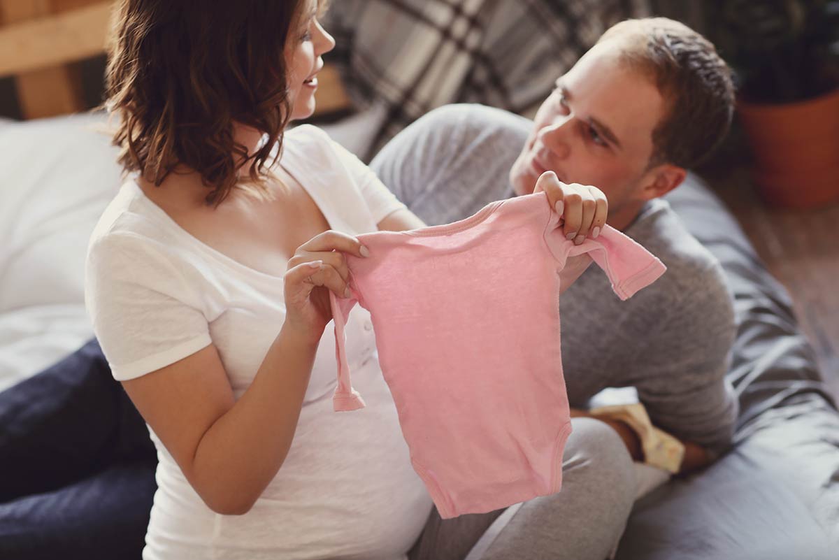 A pregnant woman and her partner are holding a pink babygro.