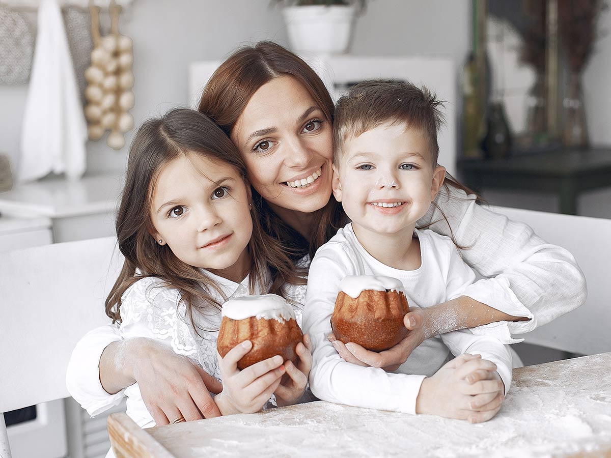 Mum smiling with her two kids who are each holding a little cake..