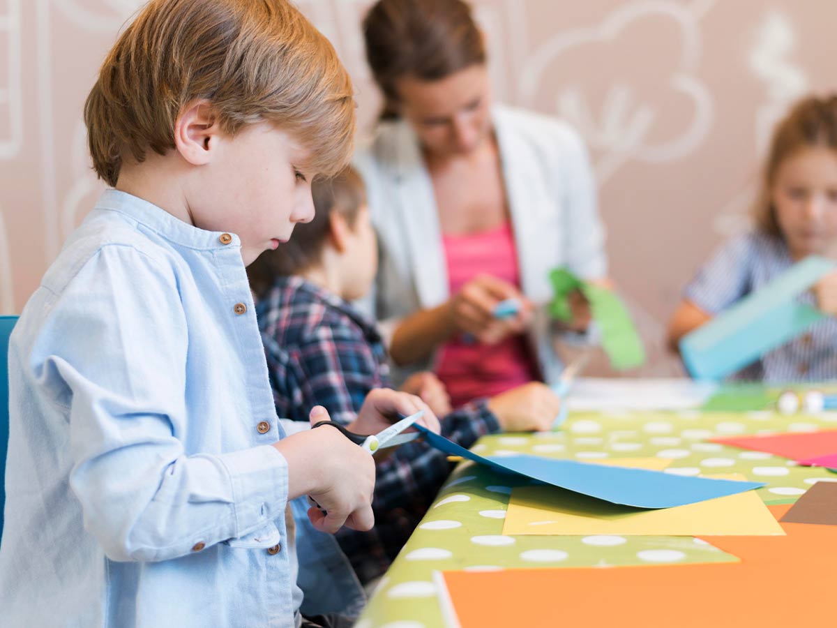 Children standing around a table cutting paper to make origami animals and koalas.