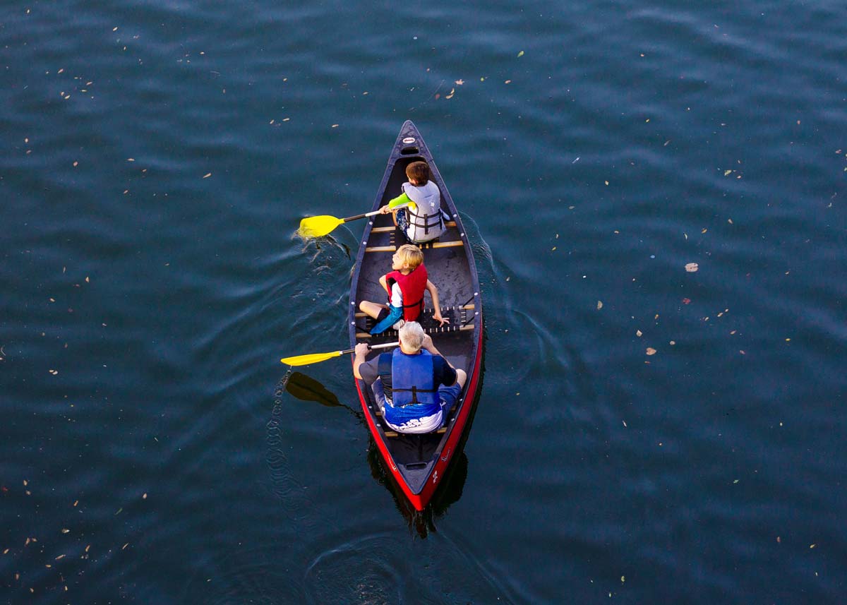 Three boys wearing life vests as they row on the water in a canoe.