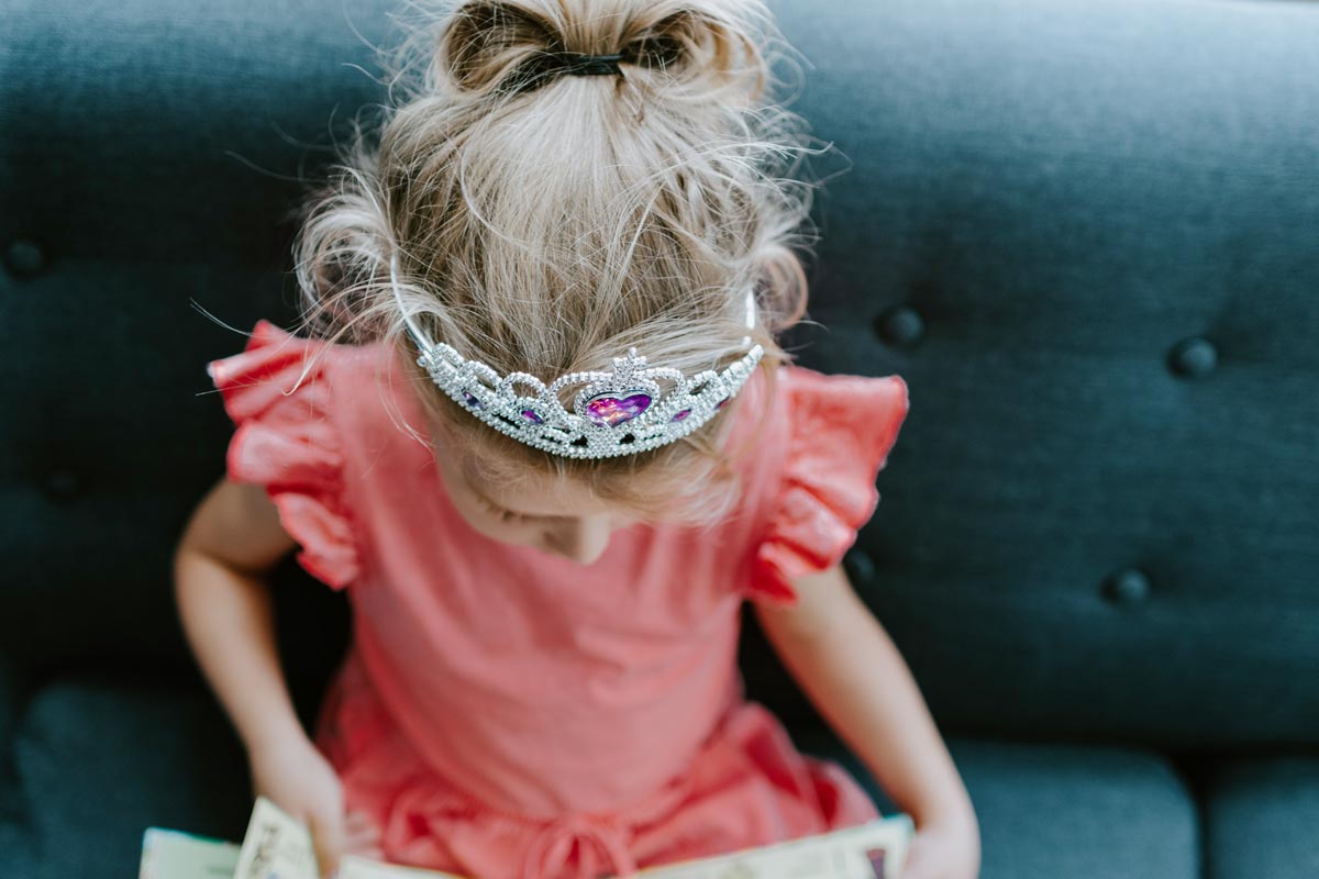 A little girl wearing a princess crown is reading a fairy tale.