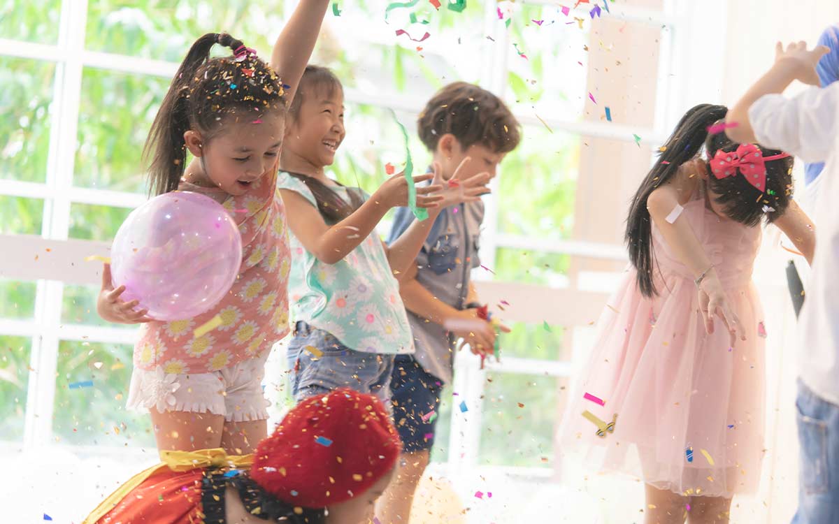 Happy kids jumping and dancing as they're showered with confetti at a birthday party.