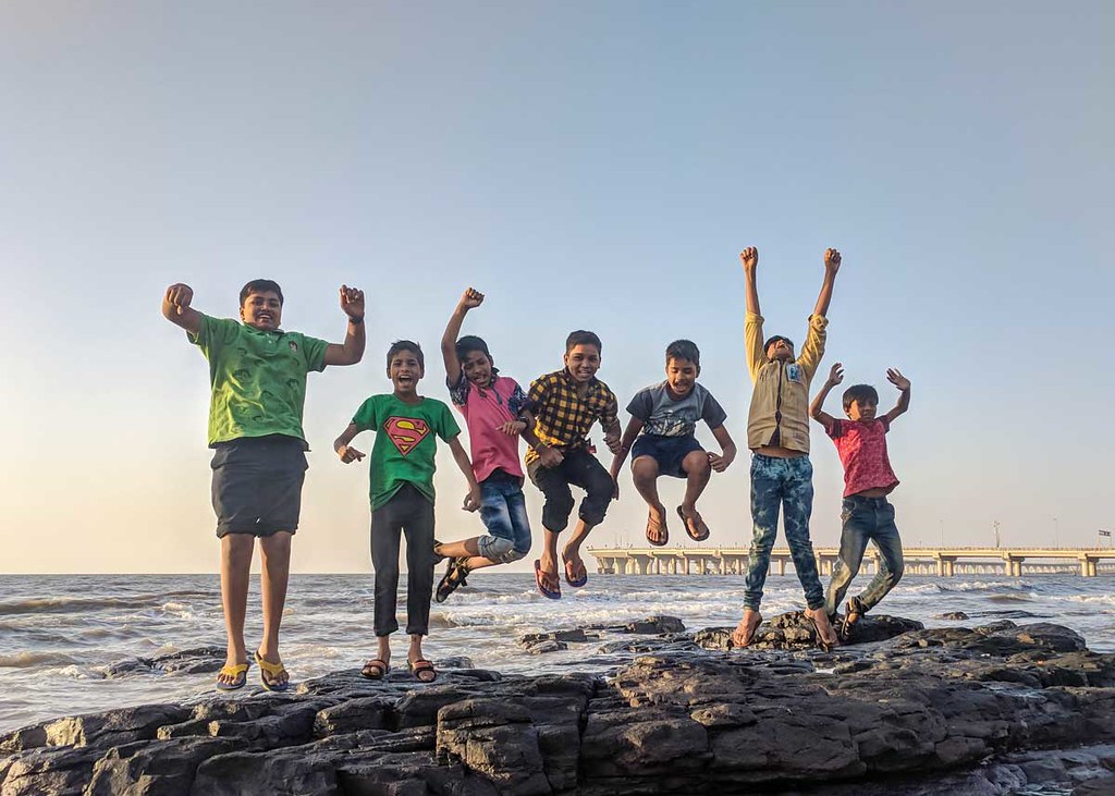 A group of young boys happily jump into the air at the beach.