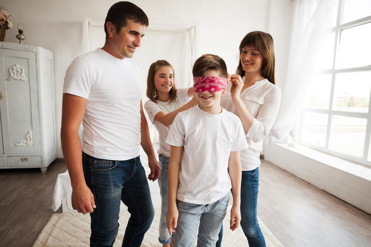 A young boy is wearing a red blindfold as he and his family play 'Who am I? riddles.
