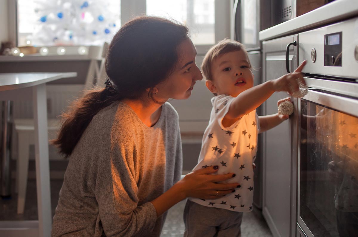Mum and her son standing in front of the over, the little boy points to the time as the dog cake is done.o