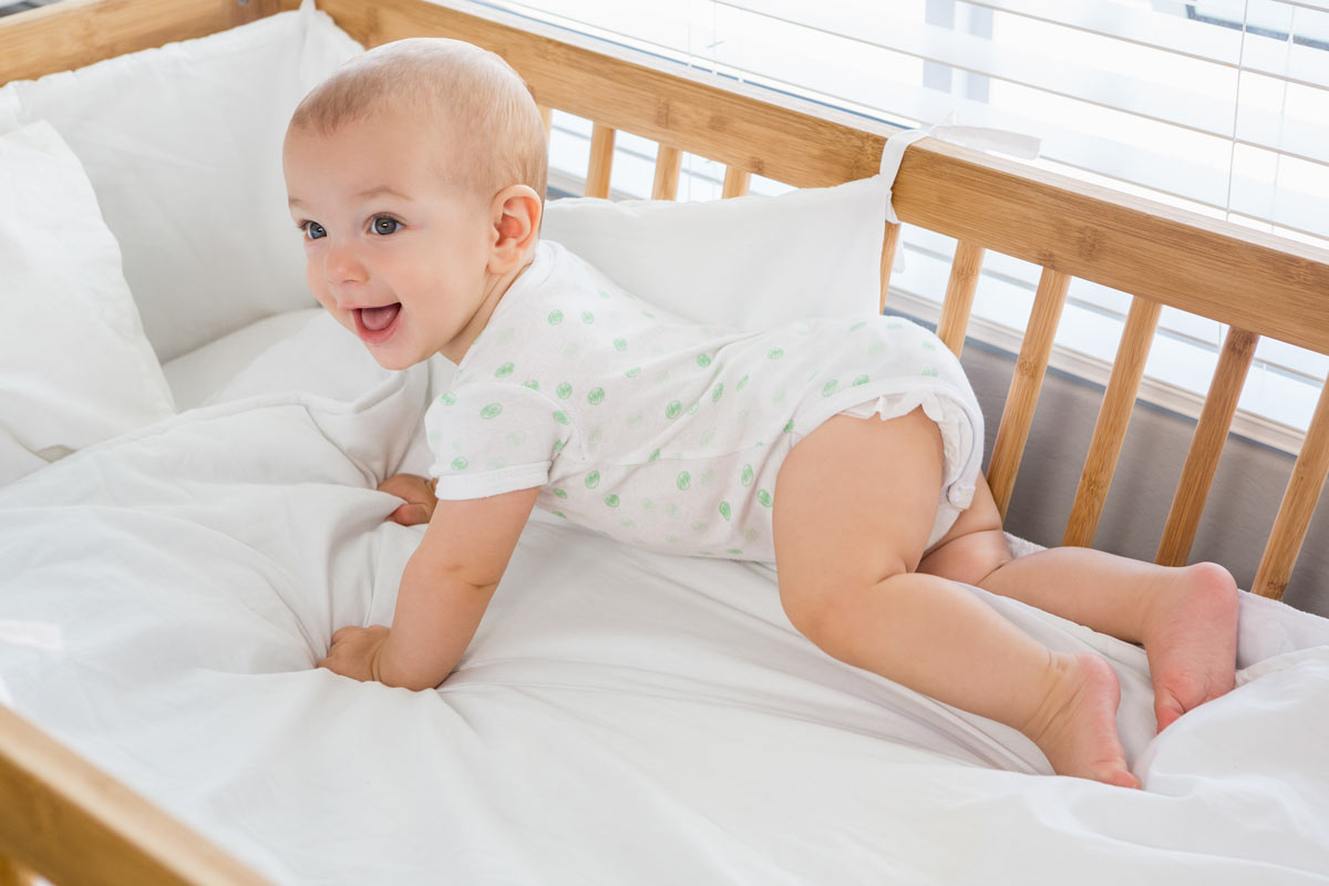 Baby boy crawling in his cot, smiling back at his parents.