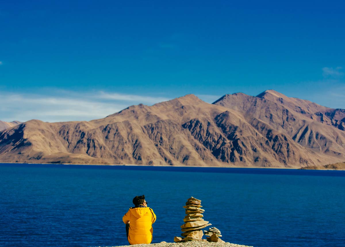Person sat near a cliff edge looking out over the lake and mountains.