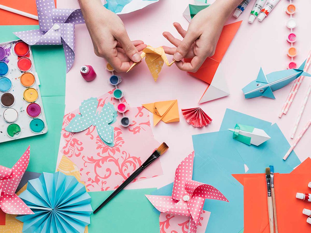 A bird's eye image of a craft table full of origami paper, models and equipment.