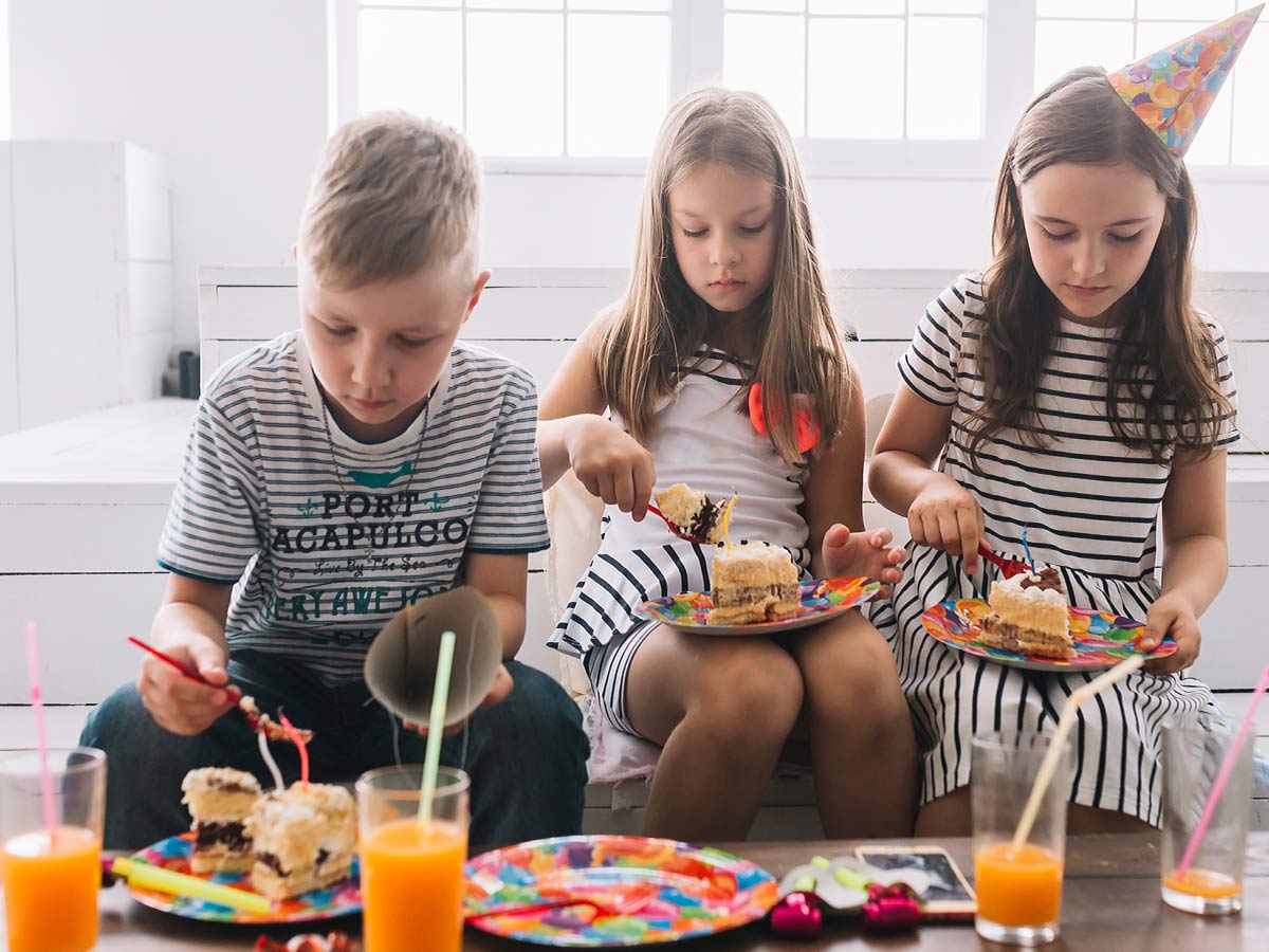 Three kids at a birthday party sat eating a slice of Fortnite cake.