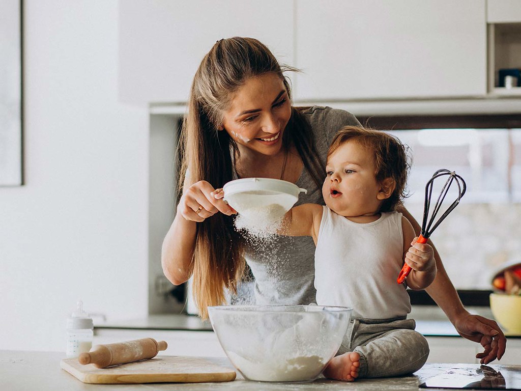 A little boy helps his mum sift flour to make a Trolls cake.