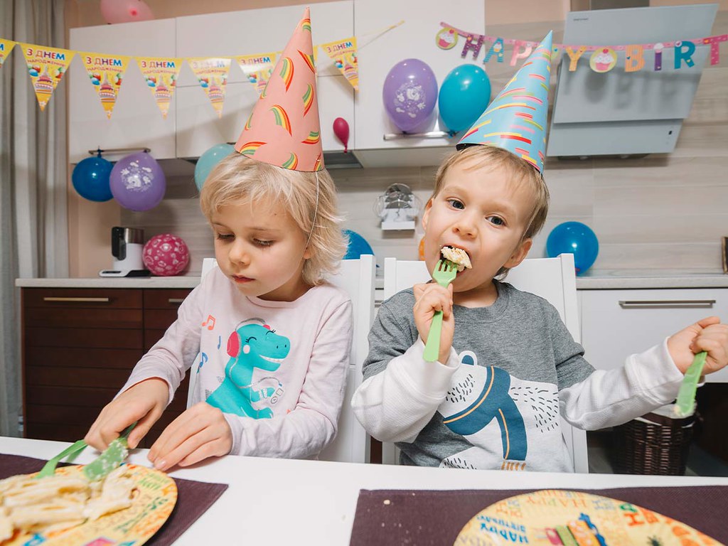 Two kids wearing party hats, enjoying a slice of cake at a birthday party.