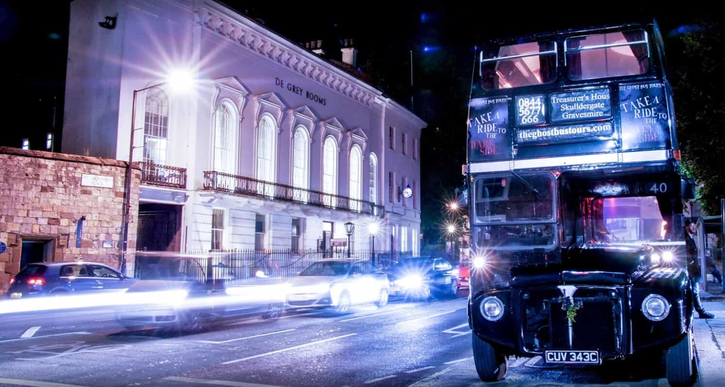 A ghost bus tour bus stopped on the street at night time.