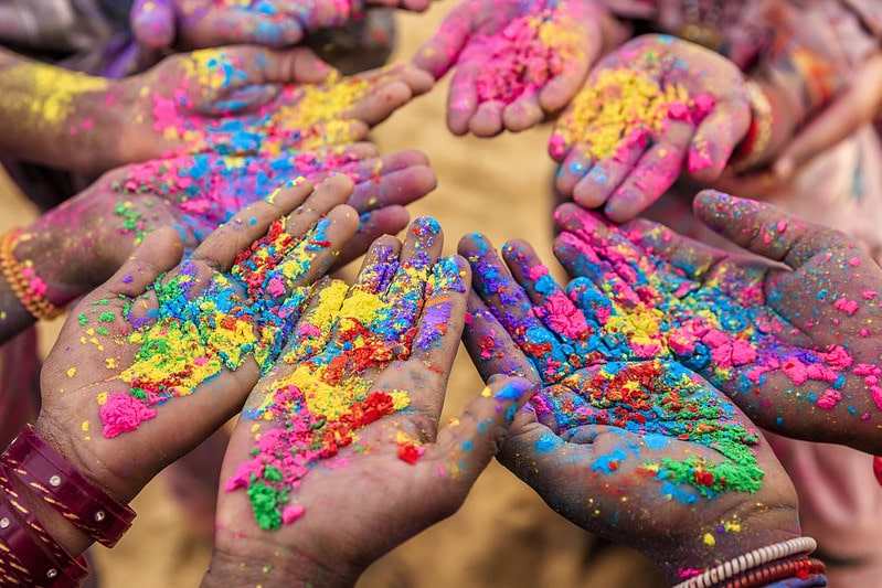 Alt text: A close up image of a group of children's hands at the Indian Holi festival.
