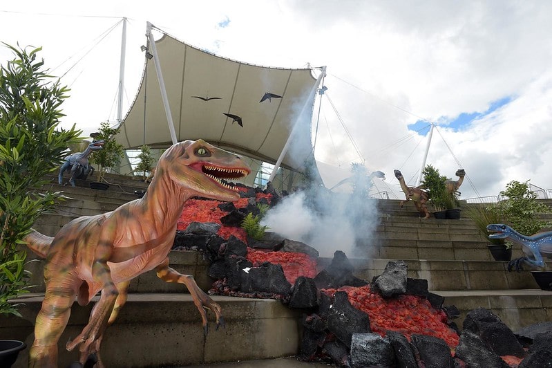 A dinosaur statue standing next to a river of lava at the Dynamic Earth museum.