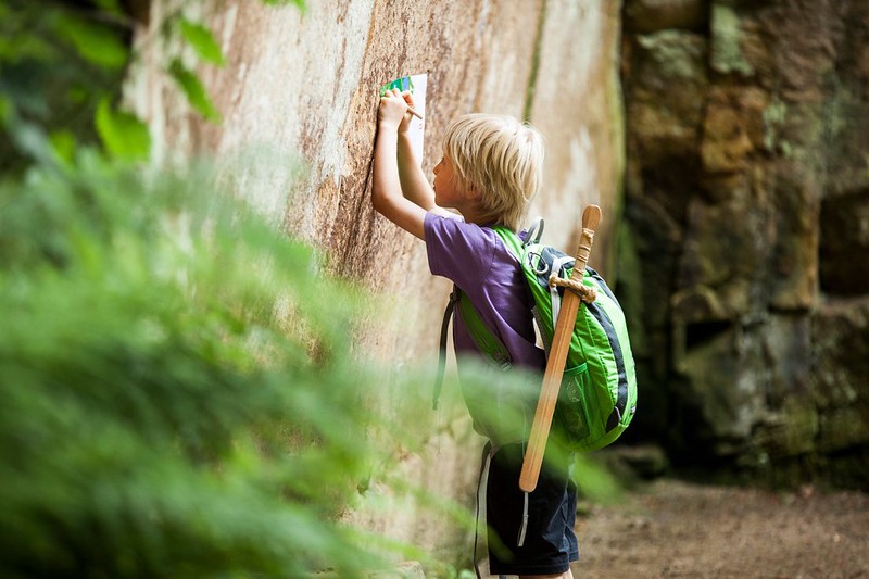 A young boy drawing on some paper whilst learning on a stone wall at Belsay Hall.