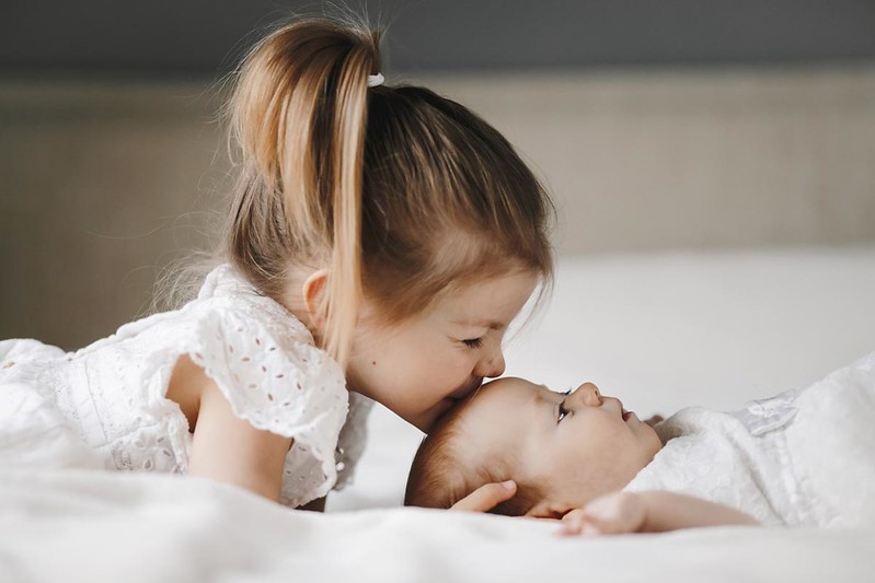 A pretty older sister fondly kissing her baby sibling.