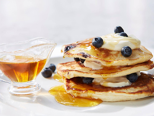 A stack of blueberry pancakes with frosting and syrup.