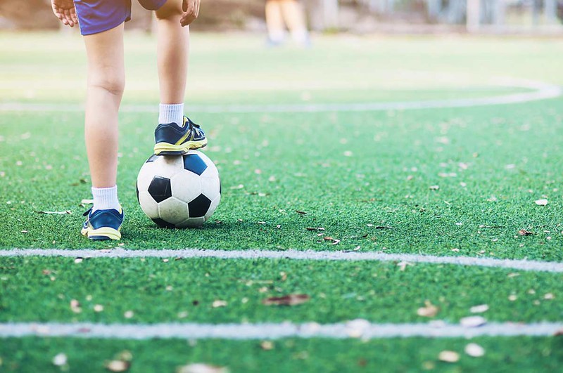 A young boy with his foot leaning on top of a football.