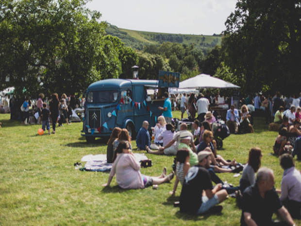 A group of people sitting on the grass at Firle Vintage Fair with vintage VW camper van in the background.