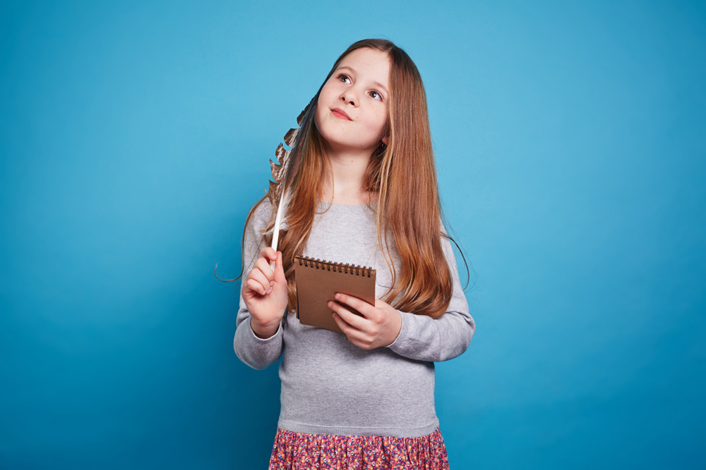 A girl looking thoughtful with her notepad against a blue background.