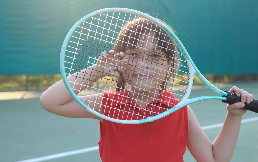A girl looking through strings on tennis racket.